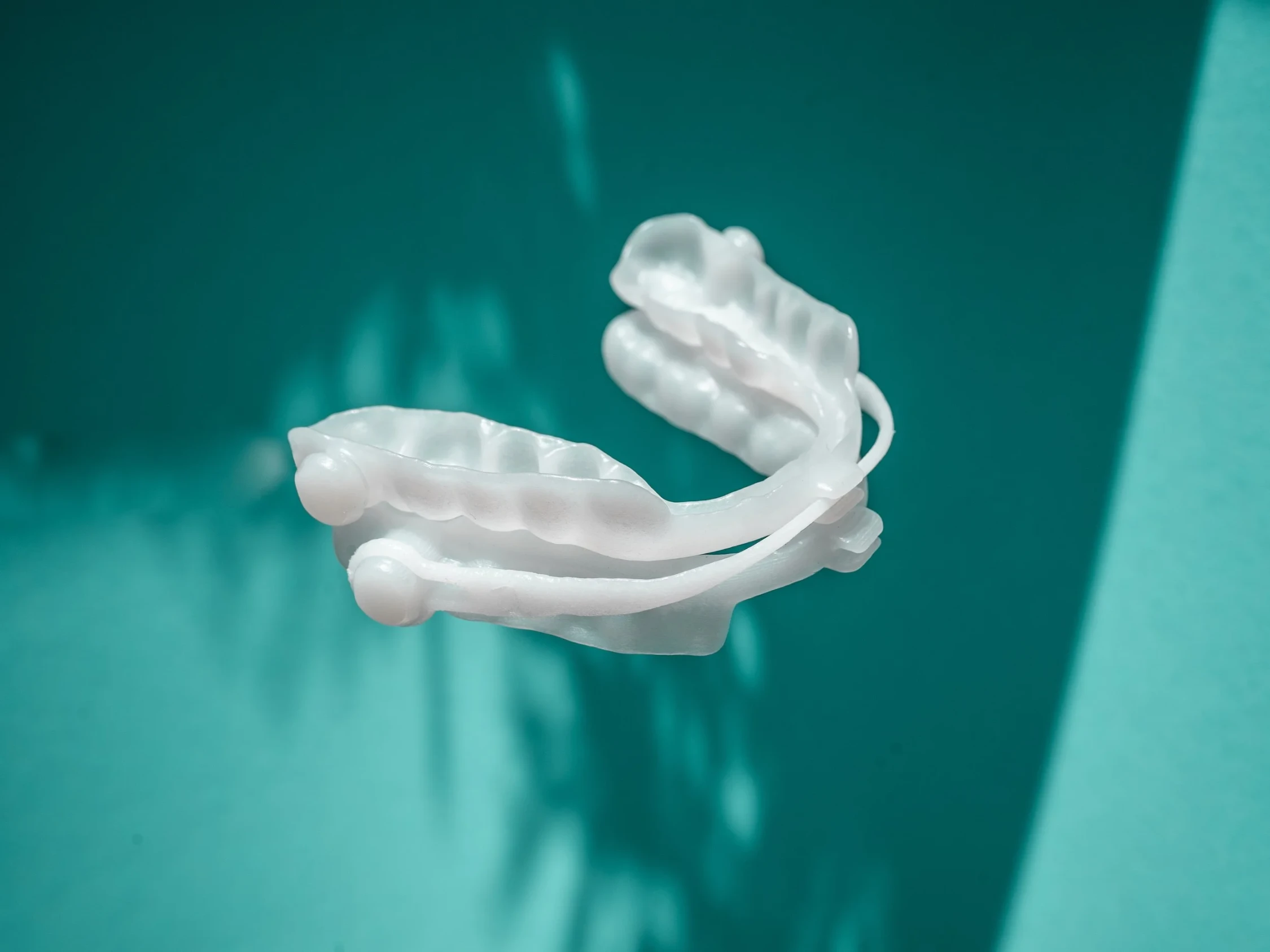 Weißes, zurückhaltendes Stück einer medizinischen Prothese oder einer kieferorthopädischen Vorrichtung auf einem blaugrünen Hintergrund.