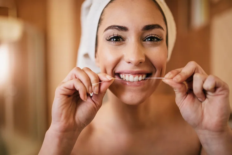 Une femme utilise du fil dentaire pour avoir une bouche saine et un sourire éclatant.
