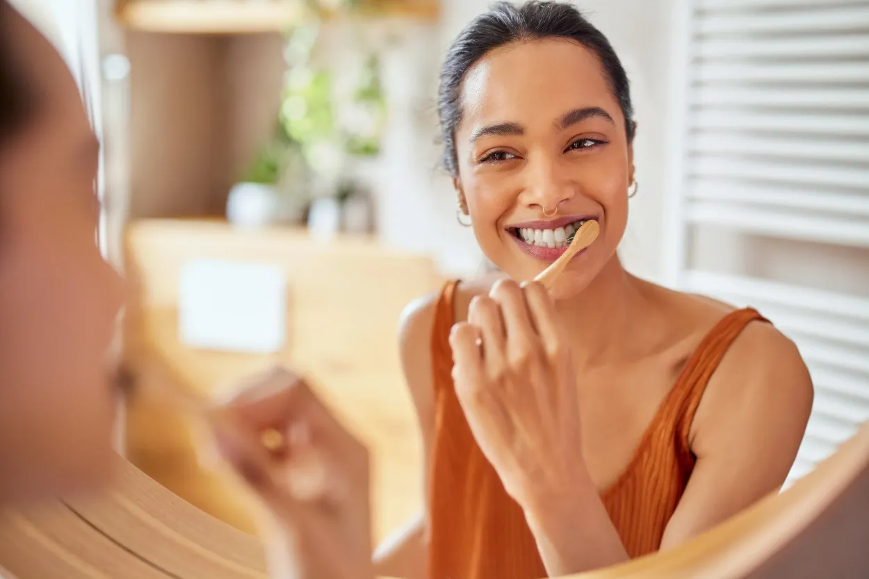 Femme souriante se brossant les dents devant un miroir.
